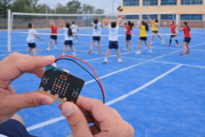 Placa micro:bit sostenida con las manos en primer plano, mientras un grupo de niños y niñas juega al voleibol en una pista escolar al fondo.